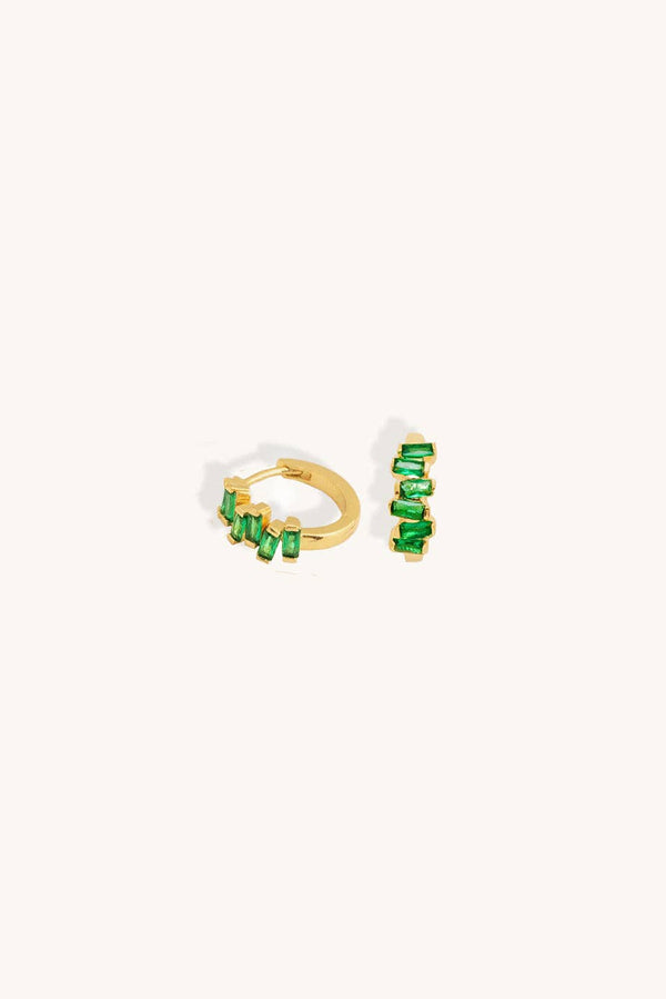 A pair of gold huggie hoop earrings embellished with baguette-cut green gemstones, displayed on a clean off-white background.