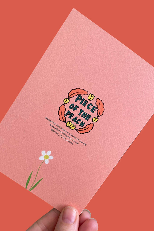 A hand holds a textured pink card featuring a retro-style illustration of a flower and the text 'PIECE OF THE BEACH' against a solid coral background.