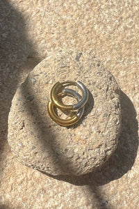 Two interlocking rings, one gold and one silver, on a textured stone surface.