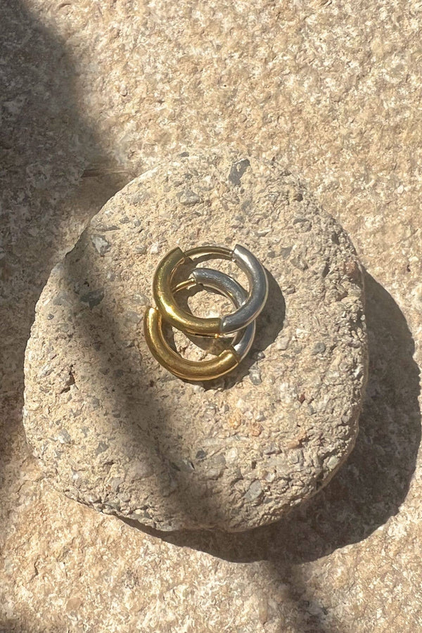 Two interlocking rings, one gold and one silver, on a textured stone surface.