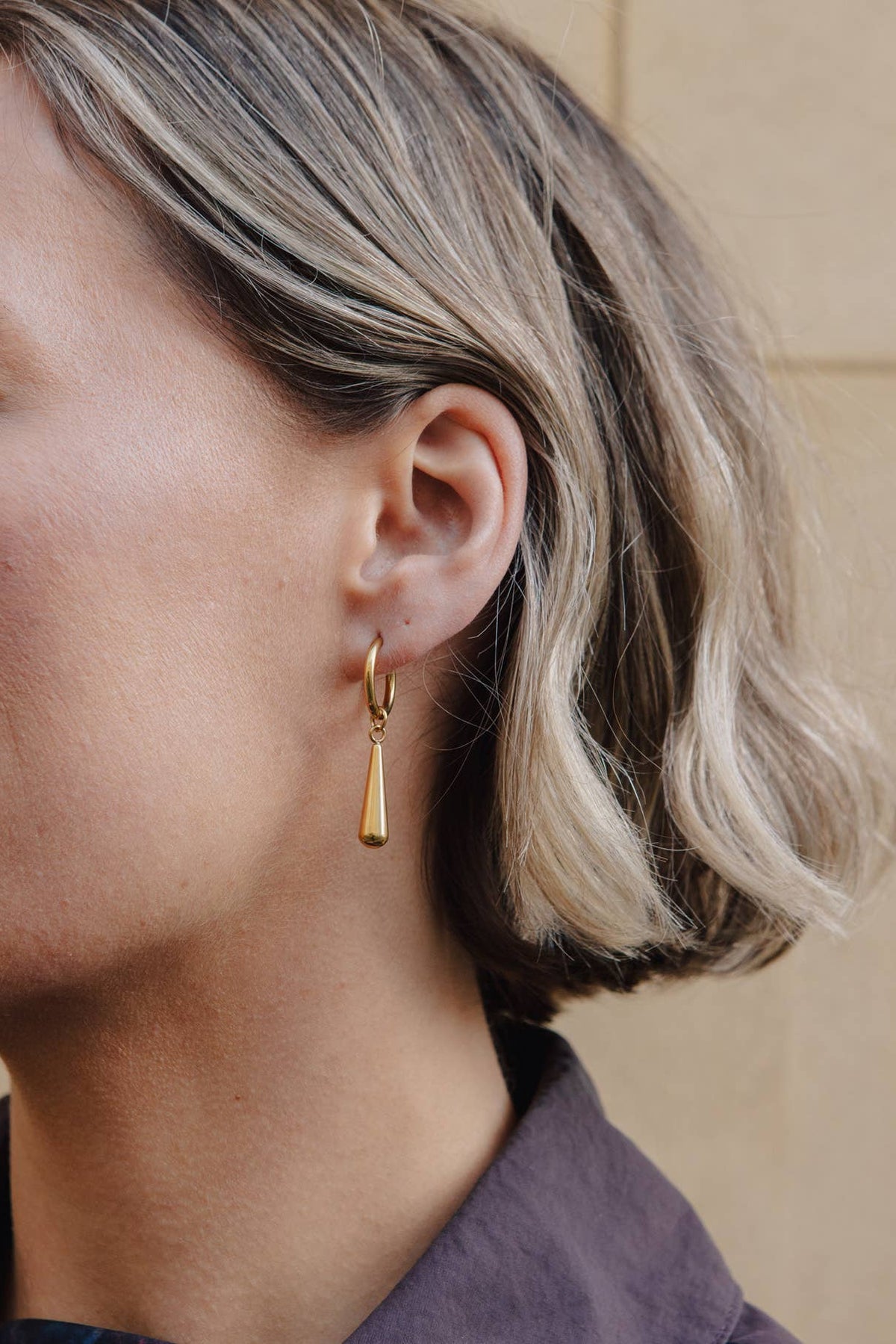 Close-up of a person wearing gold hoop earrings with a neutral background