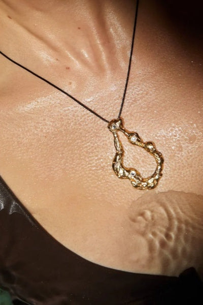 Gold necklace with a teardrop-shaped pendant on a person's neck.