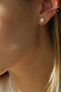 Close-up of a person wearing star-shaped earrings with a blurred green background