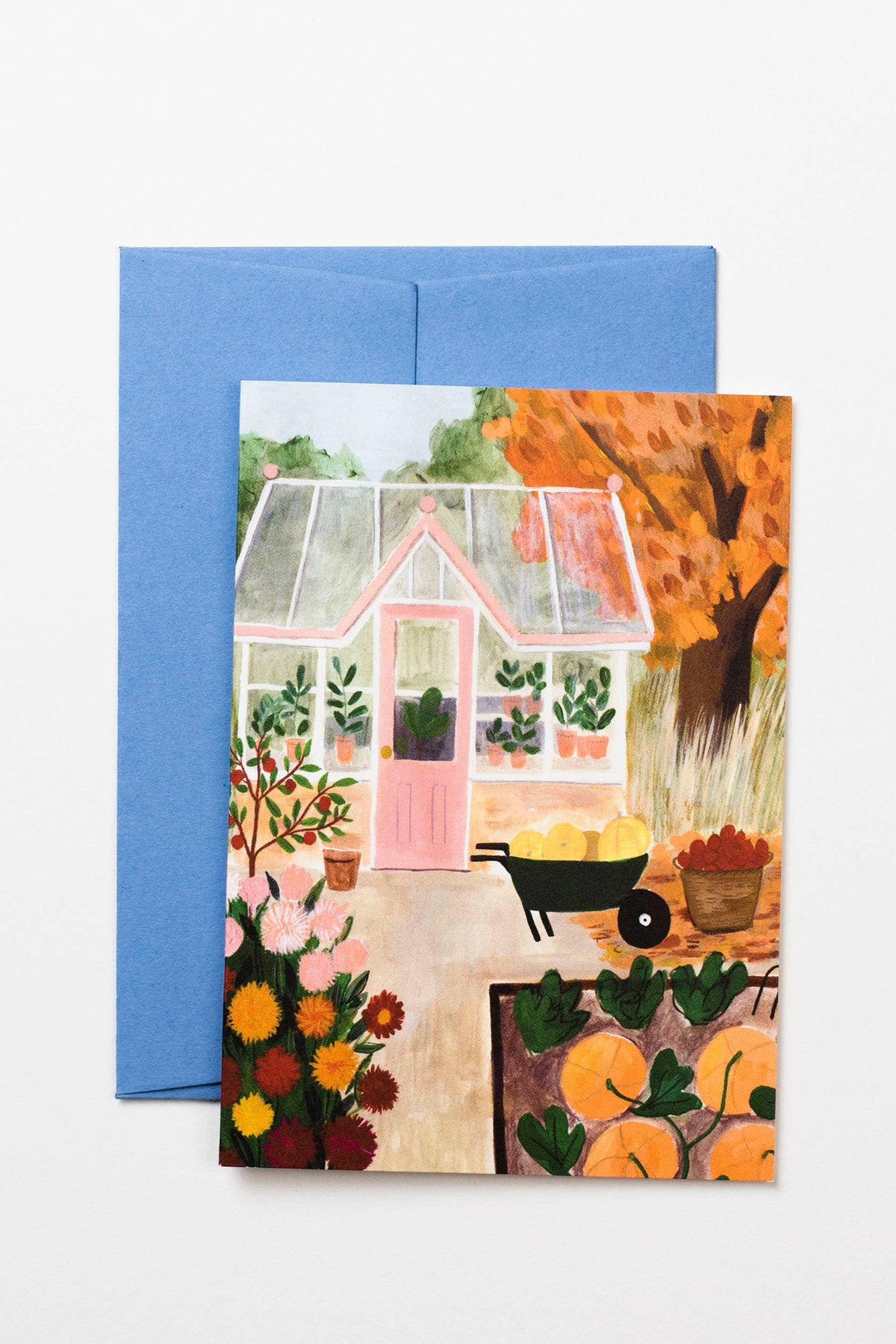 Greeting card with a colorful illustration of a house and garden, featuring pumpkins and autumn leaves, with a blue envelope.