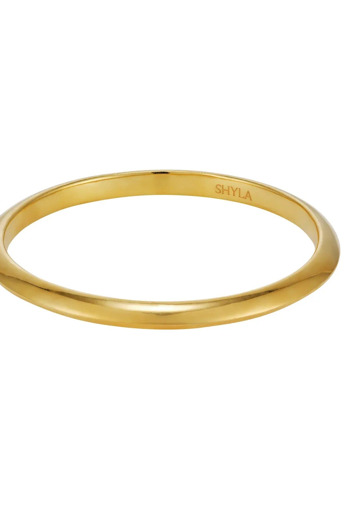 A polished yellow gold bangle bracelet with a smooth, rounded profile, featuring the brand name 'SHYLA' engraved inside the band, set against a plain white background.