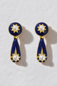 A pair of gold and navy blue drop earrings with white pearl accents, displayed on a textured white background.