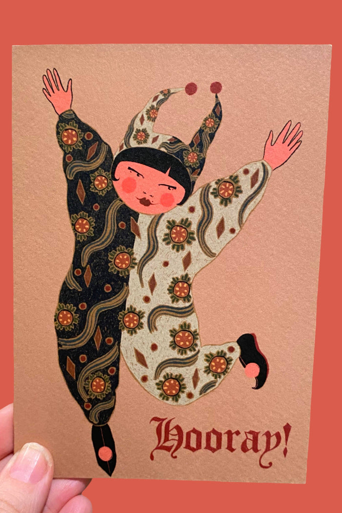 Card with an illustration of a person in a patterned outfit and 'Hooray!' text on a brown background.