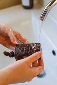 Hand washing a bar of soap under running water in a sink.