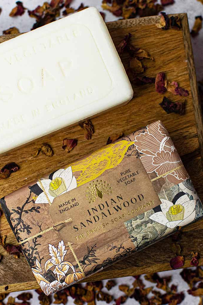 Bar of soap on a wooden block with packaging labeled 'Indian Sandalwood' surrounded by dried flowers.
