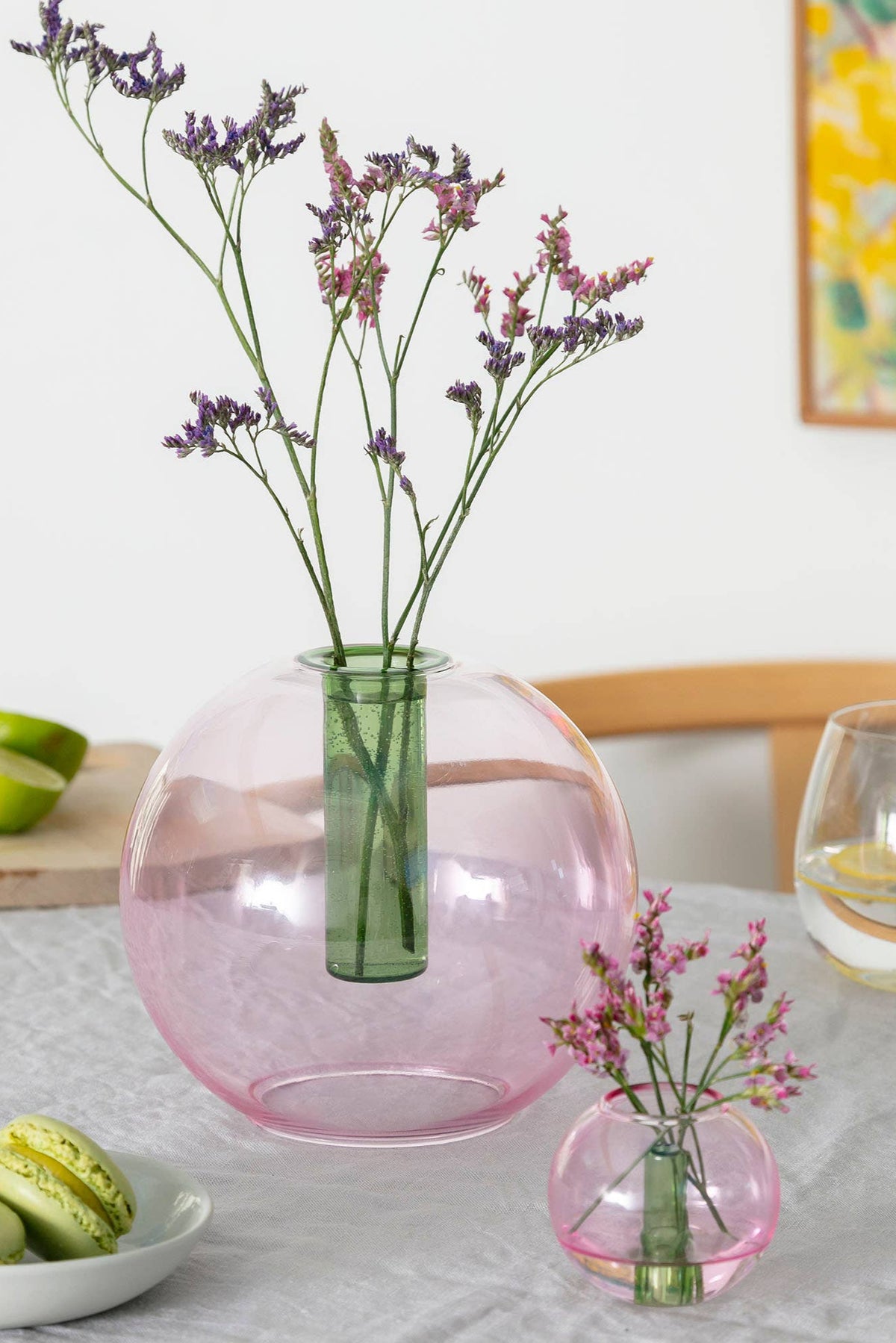 Pink glass vase with flowers on a table with limes and cookies