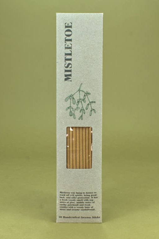 A tall, narrow rectangular box of Mistletoe incense sticks, featuring a textured off-white cover with a green mistlet illustration and a clear window showing the light brown incense sticks inside, set against a solid olive green background.