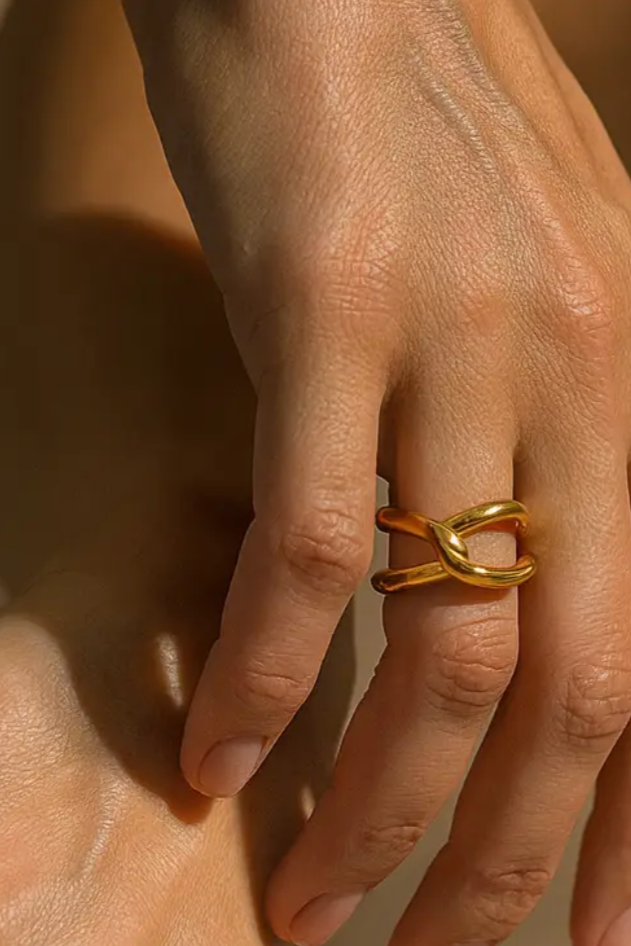 Close-up of a hand wearing a gold ring on a neutral background