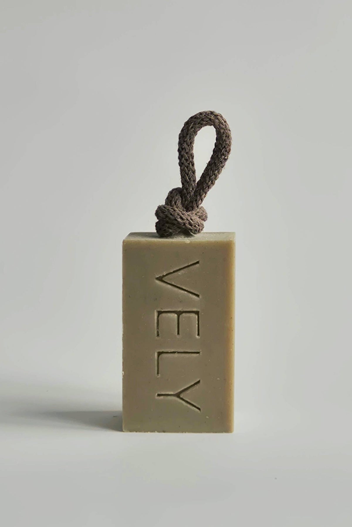 Bar of soap with a rope on a gray background, branded 'VELY'.