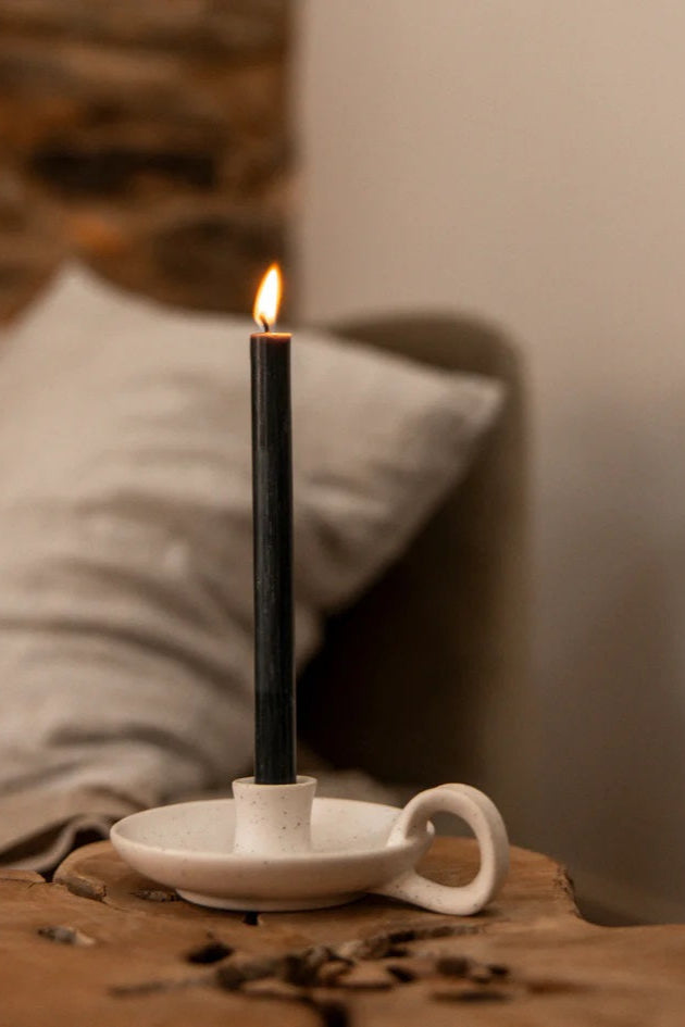 Black candle in a white holder on a wooden surface with a blurred background