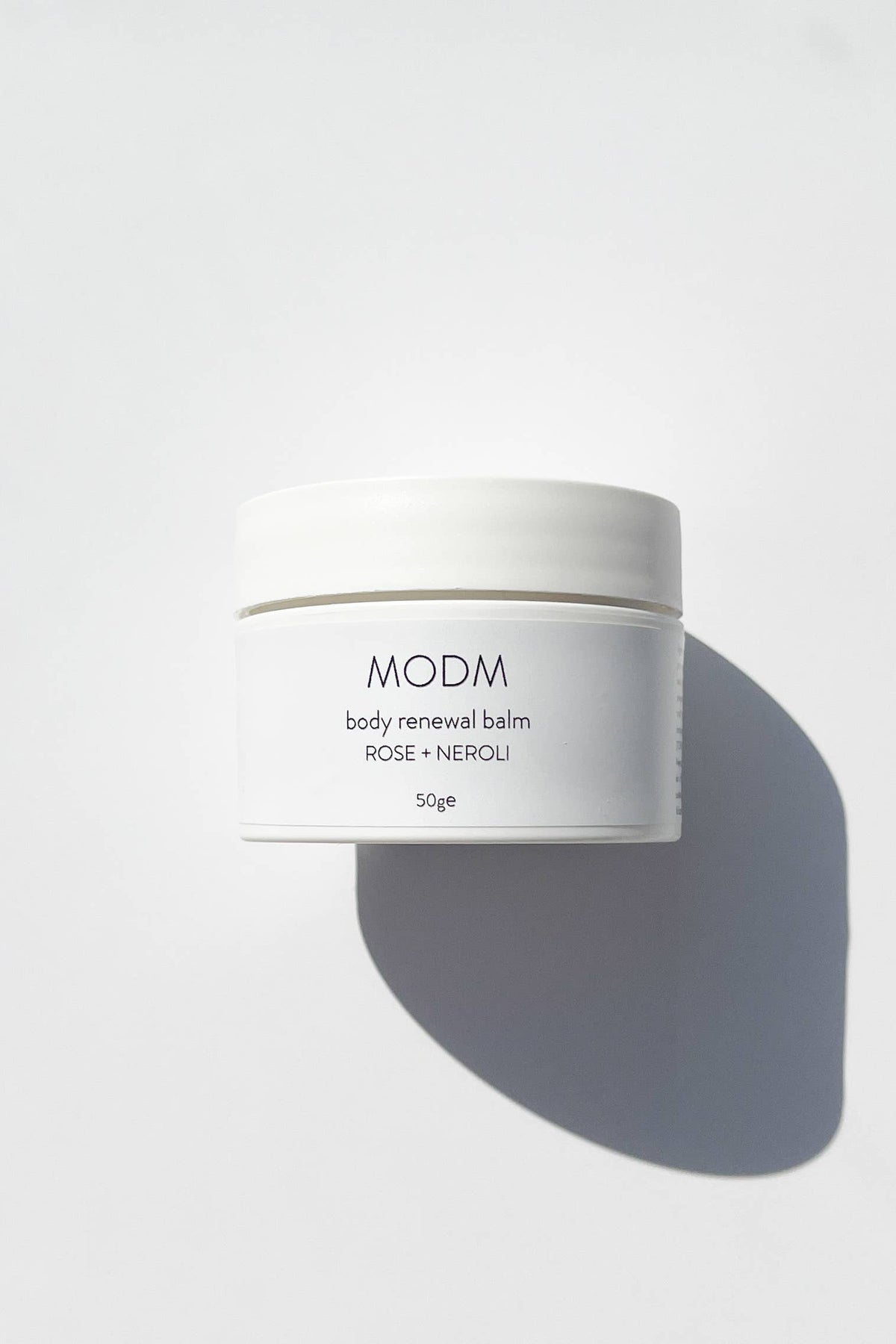 White jar of MODM body renewal balm on a light gray background