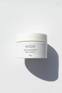 White jar of MODM body renewal balm on a light gray background