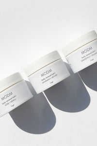 Three white jars of MOOM body renewal balm on a light gray background