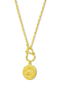 A gold necklace with a twisted chain, a small decorative ring connector, and a round medallion pendant featuring a stylized face, shown against a plain white background.