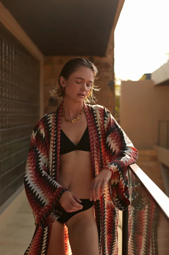 Woman in a patterned robe and black bikini standing on a balcony.