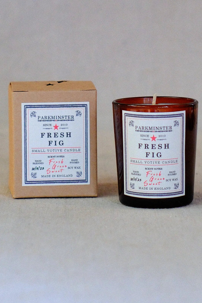 A small votive candle in an amber glass jar next to its brown cardboard box packaging, both featuring a white label with blue and red text. The brand name 'Parkminster' is clearly visible.