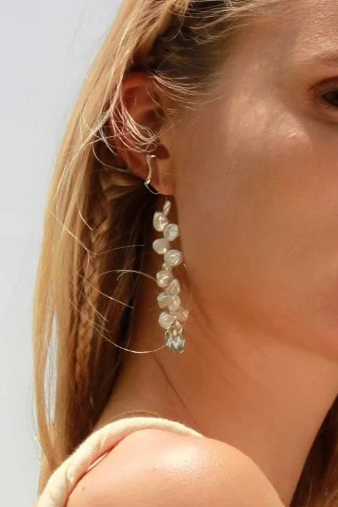 Close-up of a woman wearing pearl earrings with a neutral background