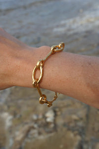 Gold chain bracelet on a wrist with a blurred natural background