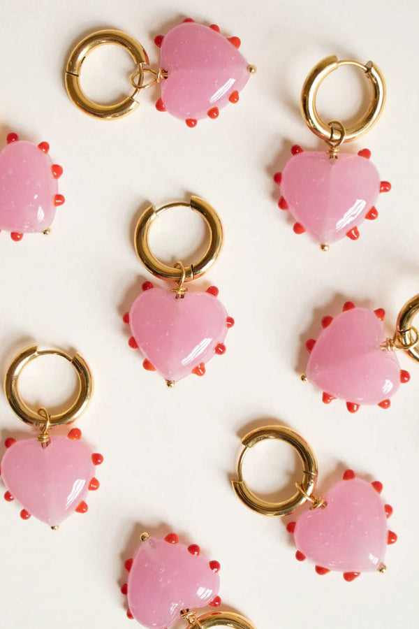 Pink heart-shaped charms with gold loops on a white background