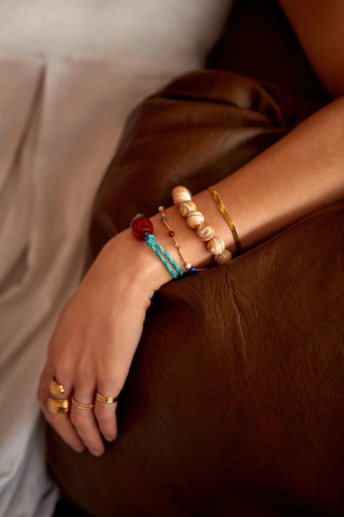Close-up of a wrist with multiple bracelets and rings on a brown surface