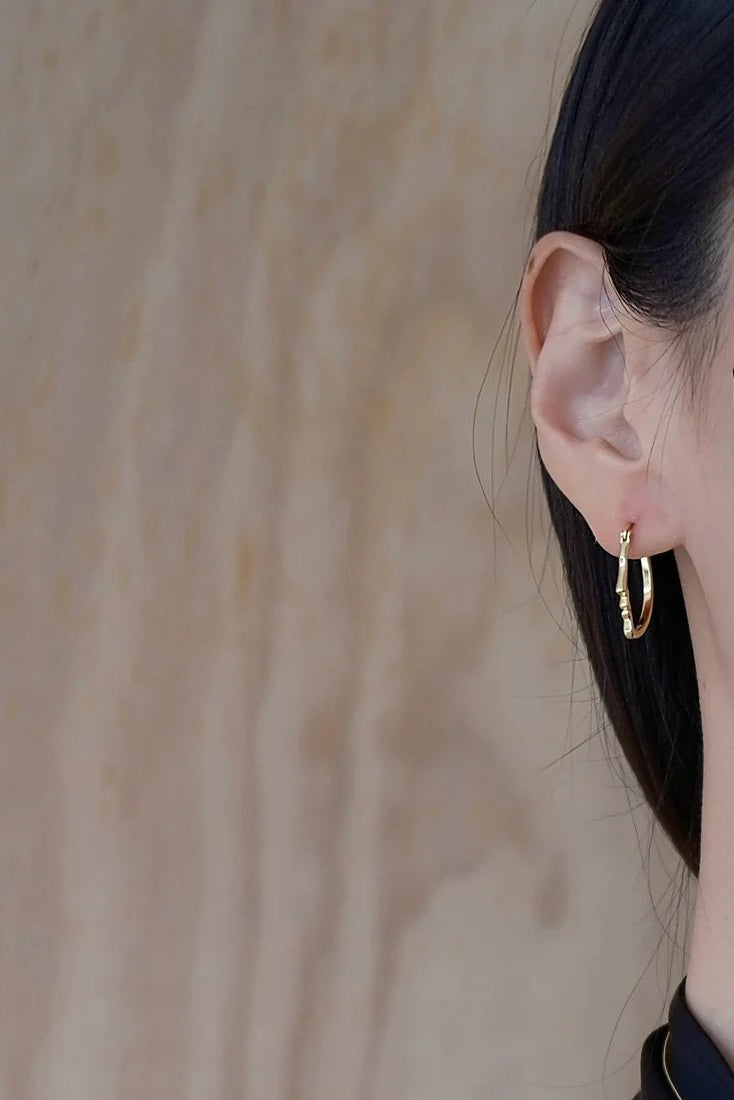 Close-up of a person wearing a gold hoop earring with a neutral background