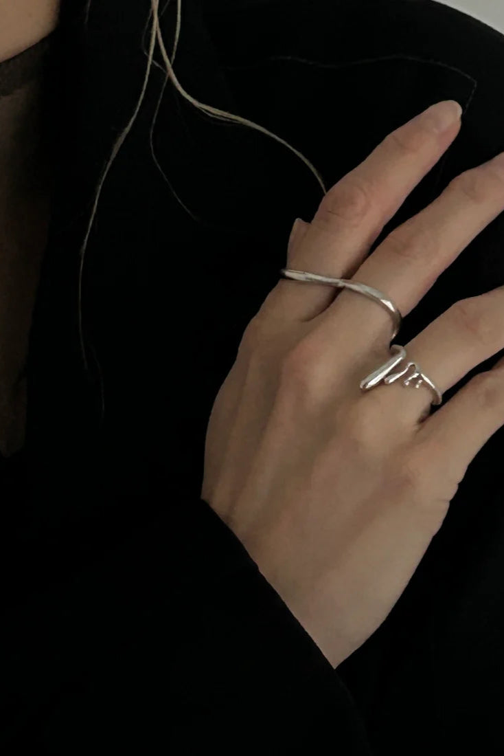 Close-up of a hand wearing two silver rings on a dark background