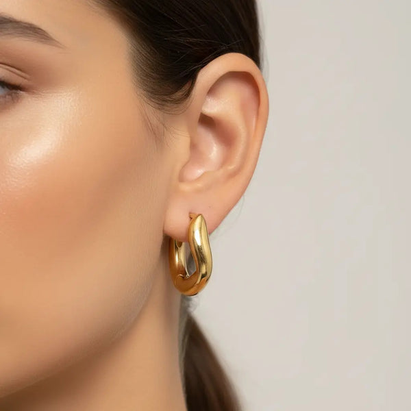 Gold hoop earring worn by a model on a neutral background